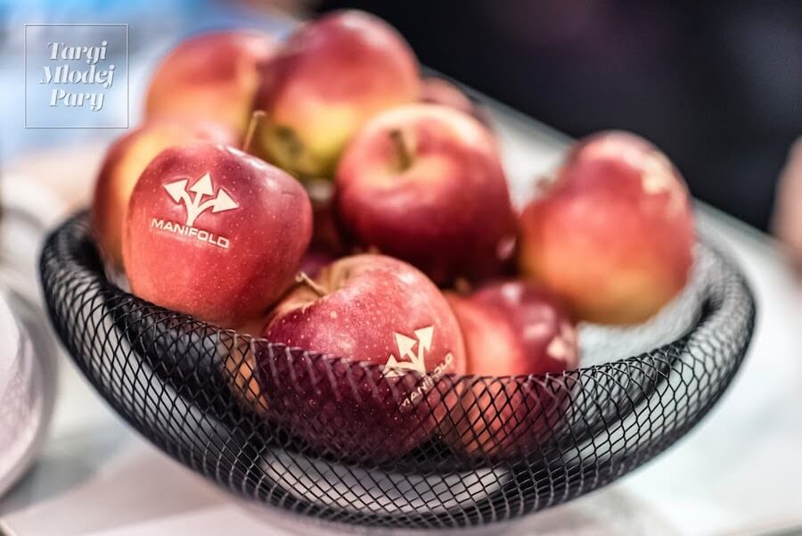 W koszyku wystawcy targów ślubnych leżą jabłka dla zwiedzających z wyrytym logo firmy.