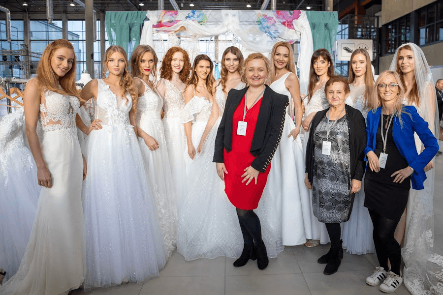 Grupa modelek w sukniach ślubnych pozuje do zdjęcia z projektantką mody ślubnej.