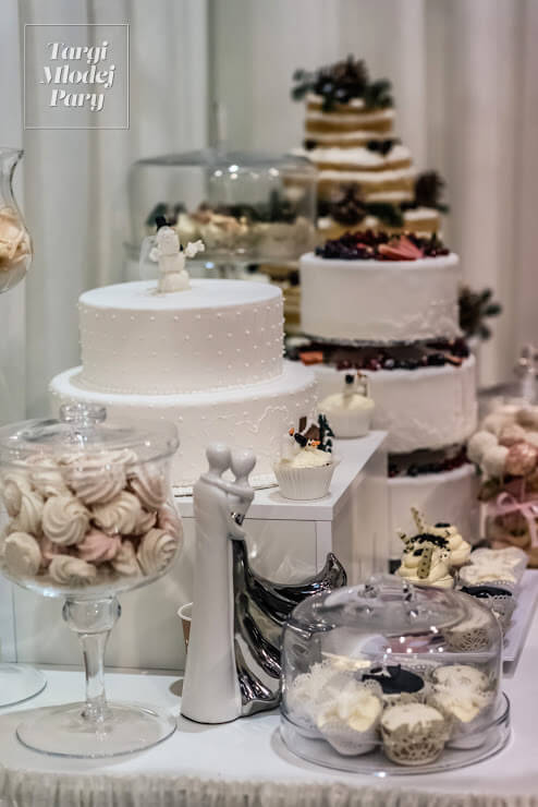 Na stoisku targów ślubnych prezentują się torty weselne oraz inne wyroby cukiernicze.